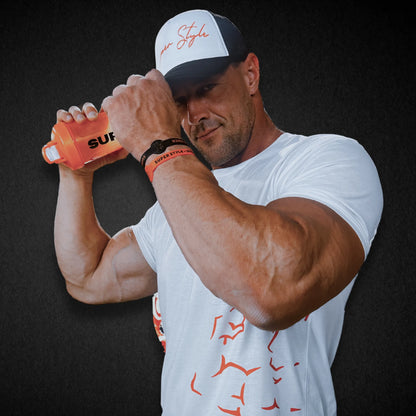 Person wearing a black super trucker hat with a white foam from labeld with a super style signature logo  hat looking foward into the camera while holding a shaker cup and showing two rubber band company bracelets 