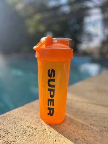 Orange shaker cup with black lettering sitting on the ground next to a pool