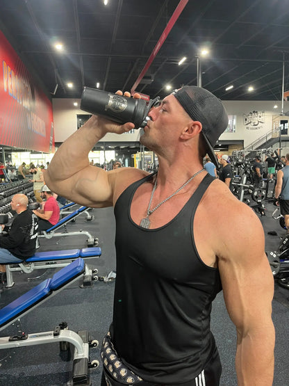 Muscular man drinking from a shaker bottle in a gym setting