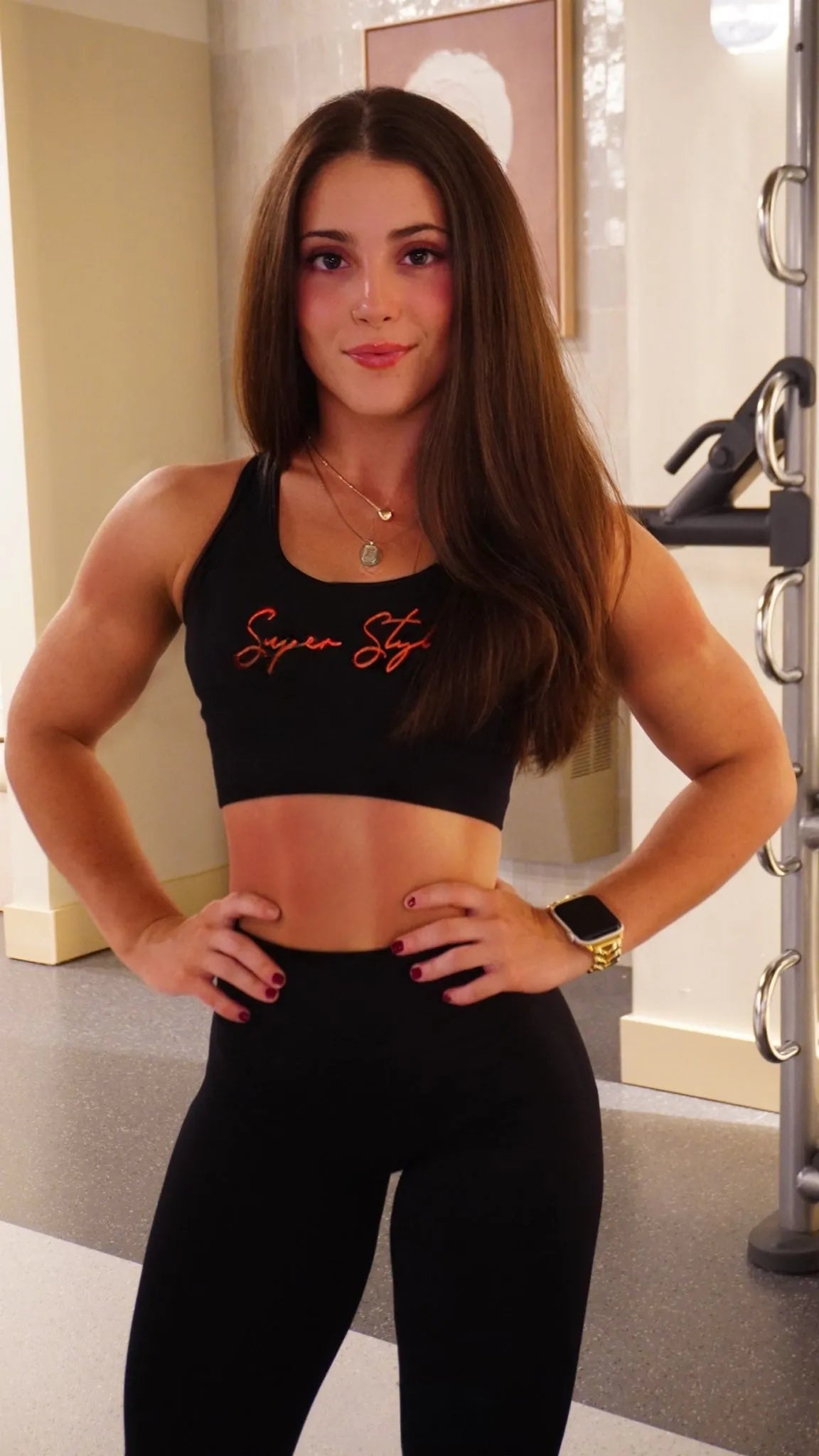 Woman wearing black Super Style activewear posing confidently in a gym setting, representing strength, fitness, and an empowered lifestyle.