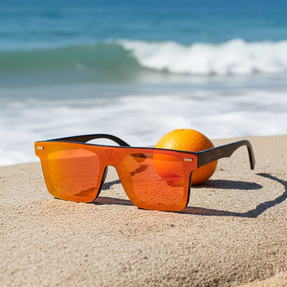 Super Style orange mirrored sunglasses resting on sandy beach beside an orange fruit with ocean waves in the background, capturing vibrant coastal lifestyle and summer fashion.