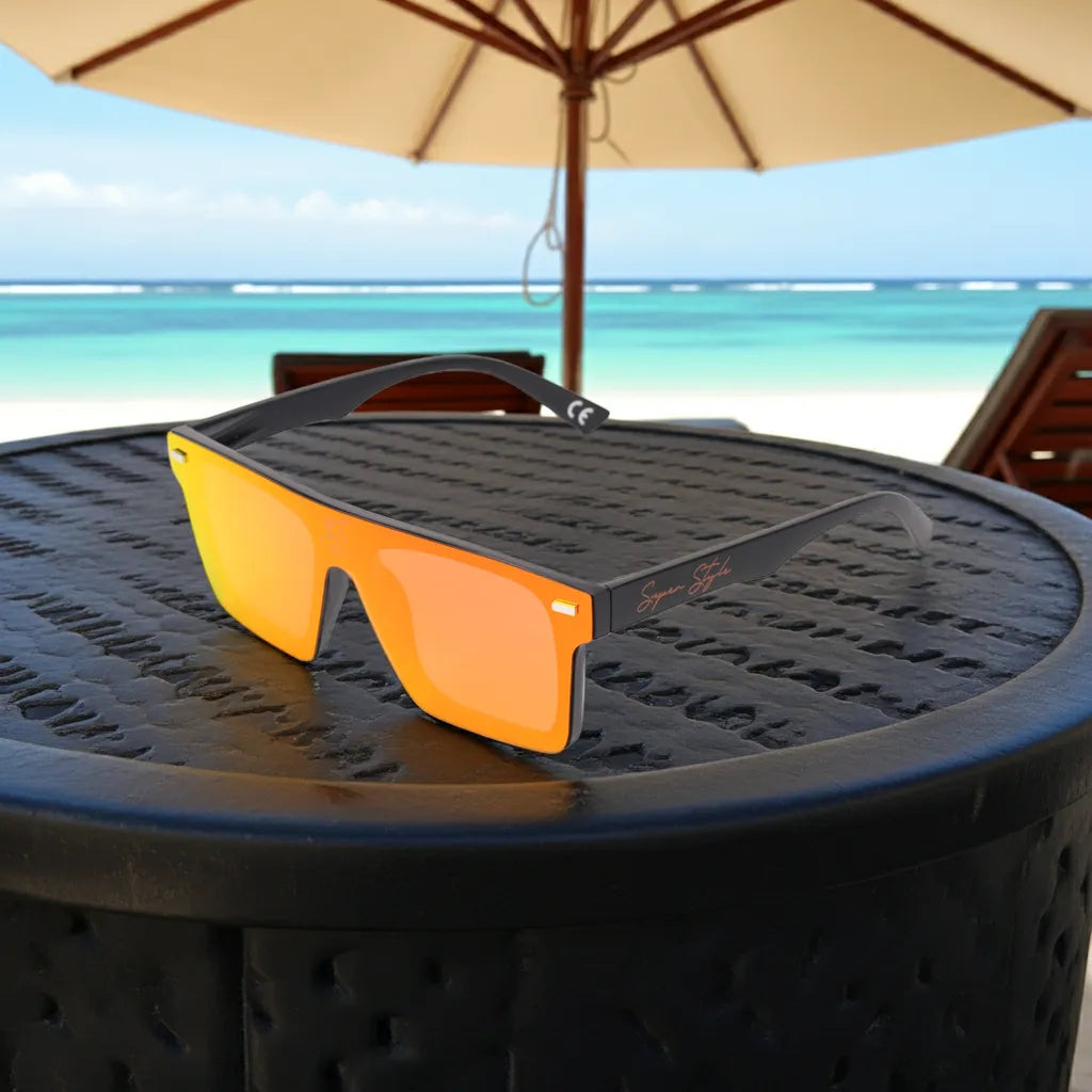 Super Style orange mirrored sunglasses placed on a round beachside table overlooking turquoise ocean water, reflecting luxury coastal lifestyle and summer fashion vibes.
